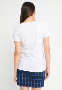 Camiseta blanca de manga corta con un corte relajado, combinada con una falda a cuadros azul marino con líneas azules. Textura de tela suave.