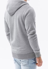 Sweat-shirt à capuche gris avec une texture douce, des poignets et un ourlet côtelés. Conçu avec une coupe décontractée, présenté de dos sur un fond blanc.