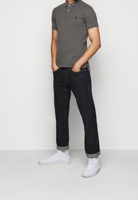 Polo grigio con colletto, abbinato a jeans scuri in denim. Sneakers alte bianche completano l'outfit casual.