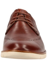 Chaussure en cuir brun avec finition lisse, bout rond et design classique à lacets. Présente des perforations décoratives sur le devant. Semelle en caoutchouc.