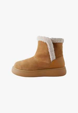 Tan suede ankle boot with a shearling collar, rounded toe, and thick rubber sole. Features a smooth back panel and contrast stitching.