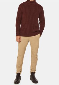 Burgundy ribbad stickad polotröja i kombination med beige chinos och svarta läderankelstövlar, vilket skapar en texturerad och lager-på-lager-look.