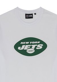 Camiseta de algodón blanca con un gráfico ovalado verde que presenta el texto "NEW YORK JETS" y un icono de fútbol en el centro. Diseño de cuello redondo.