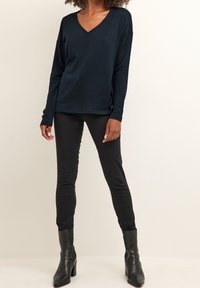 Top V à manches longues bleu marine avec une coupe décontractée, associé à un pantalon skinny noir et des bottes à talons noires. Texture lisse, design décontracté.