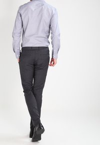 Camicia a maniche lunghe a quadri blu chiaro abbinata a pantaloni slim-fit grigio scuro e scarpe eleganti nere, vista da dietro.