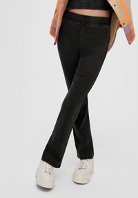 Zwarte corduroy broek met een aansluitende taille en uitlopende pijpen. Gestyled met crèmekleurige platform sneakers en onder een kleurrijke geruite jas.