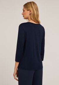 Top a maniche lunghe blu navy con scollatura rotonda e spacchi laterali. Realizzato in morbido cotone, presenta un sottile motivo a trama lungo il colletto.