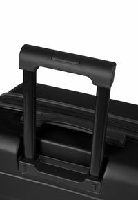 Valigia da cabina nera con superficie testurizzata, manico telescopico nero e pulsante per la regolazione dell'altezza. Chiusura con cerniera visibile.