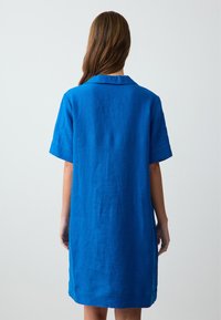 Abito in lino blu a maniche corte con vestibilità dritta e colletto, caratterizzato da una texture liscia e una lunghezza fino al ginocchio. Vista posteriore mostrata.