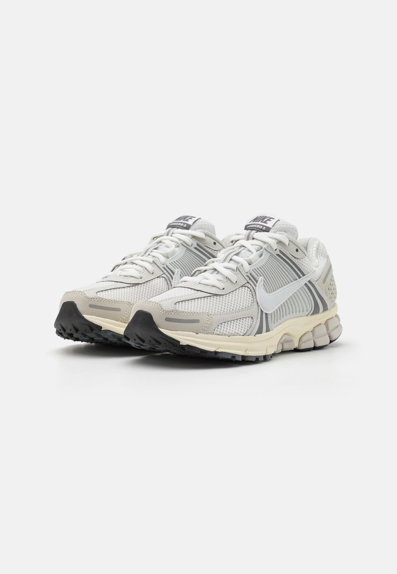 Jasnoszare, sportowe sneakersy z siateczkową cholewką, białymi akcentami i czarną gumową podeszwą. Posiadają sznurowanie i wyściółkę w okolicy kostki.