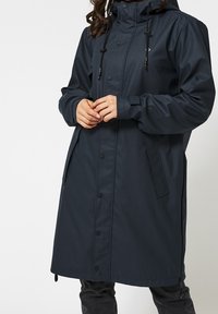 Mörkblå vattentät jacka med huva, långa ärmar, tryckknappar och dragsnören. Har sidfickor och en avslappnad passform.