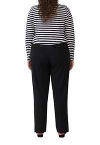 Zwarte broek met een getailleerde pasvorm, platte voorkant en twee achterzakken, gecombineerd met een marineblauw-wit gestreept shirt met lange mouwen.