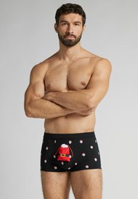 Czarne bokserki z wzorem twarzy Świętego Mikołaja i czerwoną kieszonką z tkaniny przypominającą torbę Świętego Mikołaja z przodu.