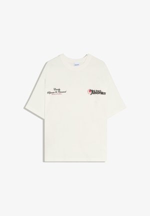 T-shirt blanc à manches courtes avec texte noir et rouge "Candy, Popcorn & Caramel" sur le côté gauche de la poitrine et "Fair & Snack favorites" sur le côté droit de la poitrine.