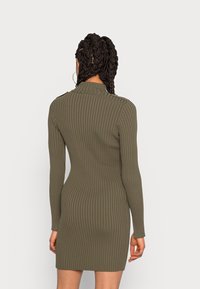 Olivgrön randig klänning med långa ärmar, muddkrage och figurnära silhuett. Slät textur med en fåll som slutar vid mitten av låret.