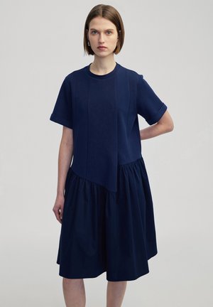Abito blu navy con un top in stile t-shirt a maniche corte e una gonna arricciata. Realizzato in tessuto morbido con una superficie liscia.