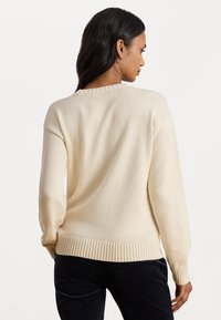 Maglione a maglia color crema con maniche lunghe, orlo a costine e finitura testurizzata. La parte posteriore presenta un collo rotondo e un design minimalista.