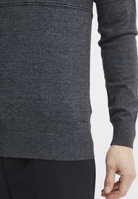 Pulover gri închis cu tiv și mânici ribbate, prezentând un model de tricotaj texturat, design ajustat și un detaliu mic cu logo pe partea inferioară.