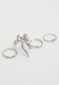 Cuatro anillos de plata dispuestos sobre un fondo blanco. Uno presenta un diseño de cinta retorcida, mientras que los otros tienen formas simples y suaves.