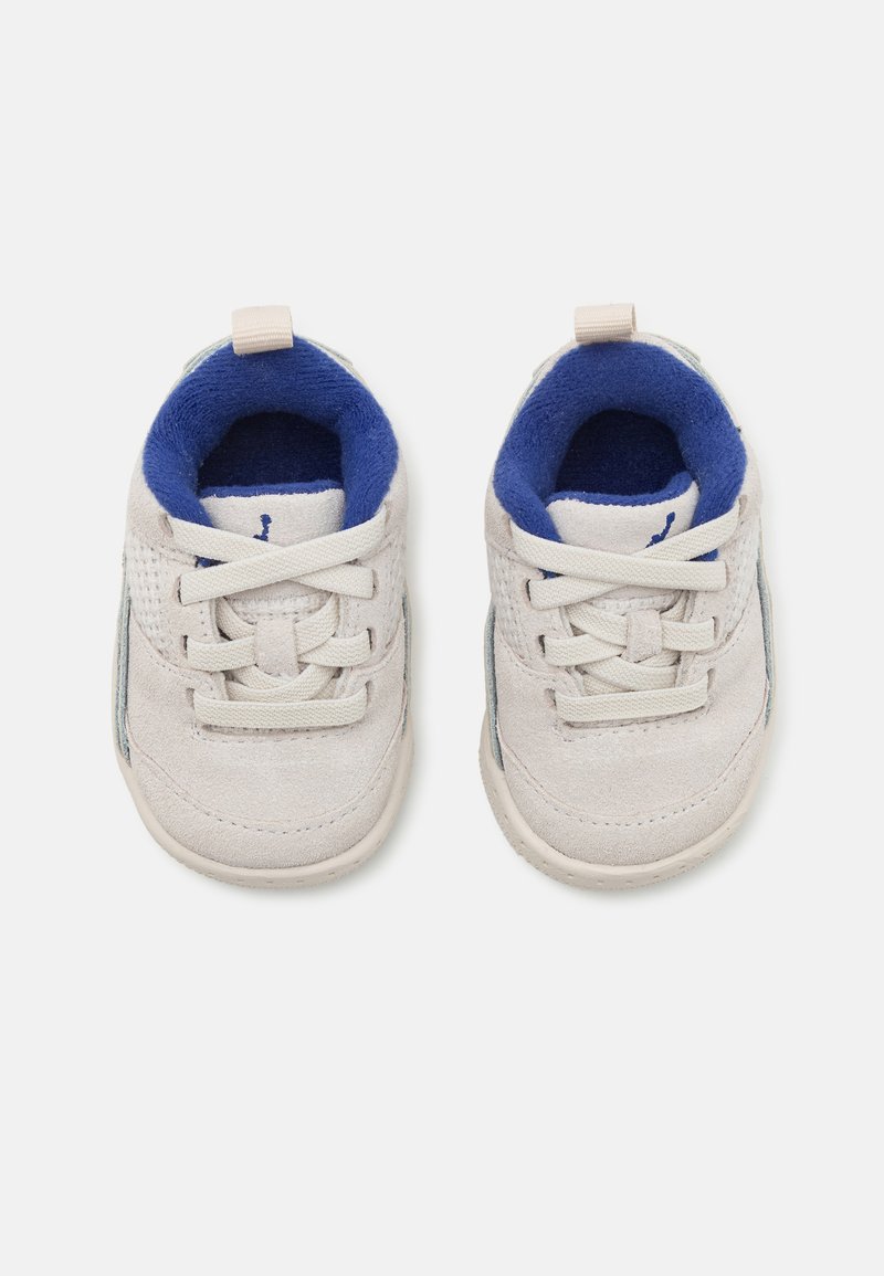 Zapatos de ante blancos con forro de tela azul, que presentan cordones y una lengüeta, puntera redondeada y acentos texturizados en los lados.