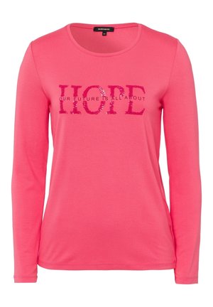 Różowa koszula z długim rękawem z okrągłym dekoltem, z cekinowym napisem "HOPE" i mniejszym napisem "OUR FUTURE IS ALL ABOUT" na wysokości klatki piersiowej.