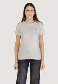 T-shirt grigio chiaro a girocollo realizzato in tessuto morbido, con un piccolo logo triangolare sul lato sinistro del petto, abbinato a jeans in denim scuro.