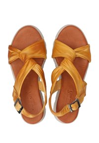 Yellow leather sandals with twisted straps, a brown footbed, and a buckle closure on the side. Textured with a smooth finish. Flat sole.