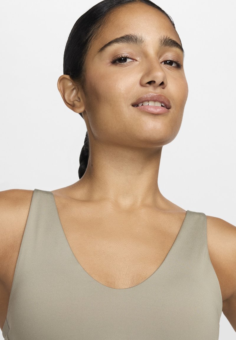 Top sin mangas de color marrón claro, con un escote profundo y una textura suave y elástica. Diseño minimalista con tirantes anchos y una forma ajustada.