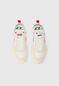 Baskets en toile blanche et en daim avec des accents rouges, semelle en caoutchouc épaisse couleur crème et lacets blancs. Comprend un logo noir et blanc sur la semelle intérieure.