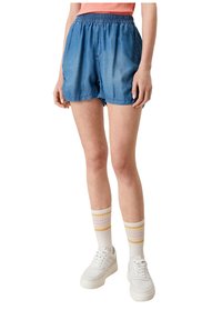 Denim shortsit, joissa on joustava vyötärö, löysä malli ja vaaleansininen väri. Yhdistetty valkoisiin nilkkasukkia ja raidallisiin nilkkasukkiin.