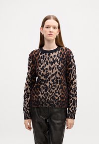 Pull en imprimé léopard avec des couleurs beige, marron et noir, col rond et manches longues, assorti à un pantalon en cuir noir.