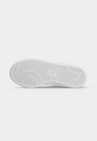 Podrážka bielej tenisky Adidas s včelím plástom a logom Adidas v strede, zobrazená na hladkom pozadí.