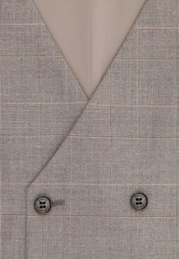 Zbliżenie na beżową, dwurzędową marynarkę w kratę z dwoma ciemnymi guzikami i klapą w kształcie litery V.