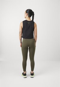 Svart ermeløs crop topp med teksturdetaljering, kombinert med olivengrønne høyhåndledds leggings og svarte sneakers med gule detaljer.