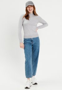 Un pull col roulé gris clair avec des accents de boutons, associé à un jean bleu à coupe ample. Porté avec une casquette grise et des baskets blanches.
