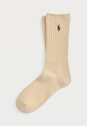 Ett par beige räfflade strumpor med crew-längd och en liten mörkbrun broderad polo-spelare-logotyp nära toppen av skaftet.
