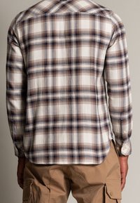 Långärmad rutiga skjorta i beige, marinblå och brun. Lätt, texturerat bomullstyg. Har knäppbara manschetter och en rundad fåll.