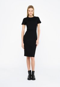 Abito nero aderente con maniche corte, lunghezza al ginocchio e scollo rotondo. Abbinato a stivali alla caviglia, con una superficie liscia e design minimale.