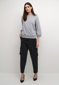 Pullover grigio in cotone con maniche lunghe e a sbuffo, abbinato a pantaloni cargo neri baggy con tasche laterali, indossato con tacchi neri.