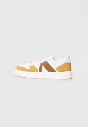 Witte sneaker met tan en bruine suede accenten, voorzien van een gladde bovenkant, vetersluiting en een gestructureerde rubberen zool.