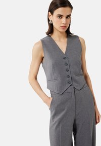 Gilet grigio su misura con scollo a V profondo, sei bottoni e tasche laterali; abbinato a pantaloni a gamba larga coordinati, realizzati in tessuto testurizzato.