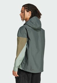 Water-resistant jacket with a hood; features green, beige, and teal color blocks; smooth texture; adjustable cuffs; minimal design.