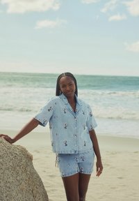 Set co-ord din denim bleu deschis, compus dintr-o cămașă cu mânecă scurtă și nasturi și șorturi, decorate cu un imprimeu floral, cu o suprafață texturată și un croi lejer.