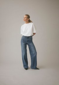 White, oversized t-shirt and blue wide-leg jeans. The jeans have a high waist and are paired with pointed black shoes. Simple, casual design.