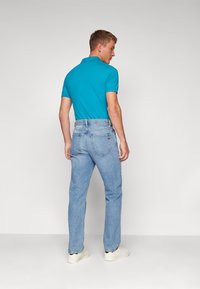 Meeste smaragdroheline polo-särk, mis on kombineeritud helesiniste teksadega. Polos on krae ning teksadel on klassikaline viie tasku disain koos nähtava õmblusega.