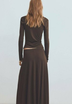 Hnedý top s dlhým rukávom skombinovaný s voľnou hnedou maxi sukňou. Materiál vyzerá mäkko; dizajn obsahuje priliehavý korzet a voľný strih.