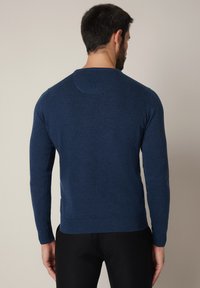 Granatowy sweter wykonany na drutach, z długimi rękawami, okrągłym dekoltem, ściągaczami na mankietach i dole. Gładka faktura z subtelnymi, jasnymi odcieniami i minimalistycznymi zdobieniami.