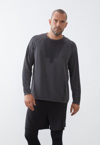 Donkergrijze lange mouw sportshirt met een textuurpaneelontwerp en ronde halslijn, gecombineerd met zwarte shorts. Smooth stof, ruime pasvorm.