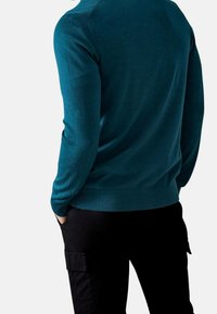 Maglione teal con maniche lunghe, scollo rotondo e polsini a coste, abbinato a pantaloni cargo neri con tasche laterali.
