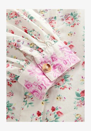 Lille lillede, mis on valmistatud valgest kangast, millel on punased, roosad ja rohelised lilled; kokku volditud varrukad ja roosa lillemustriga krae, millel on ümmargune nupp.